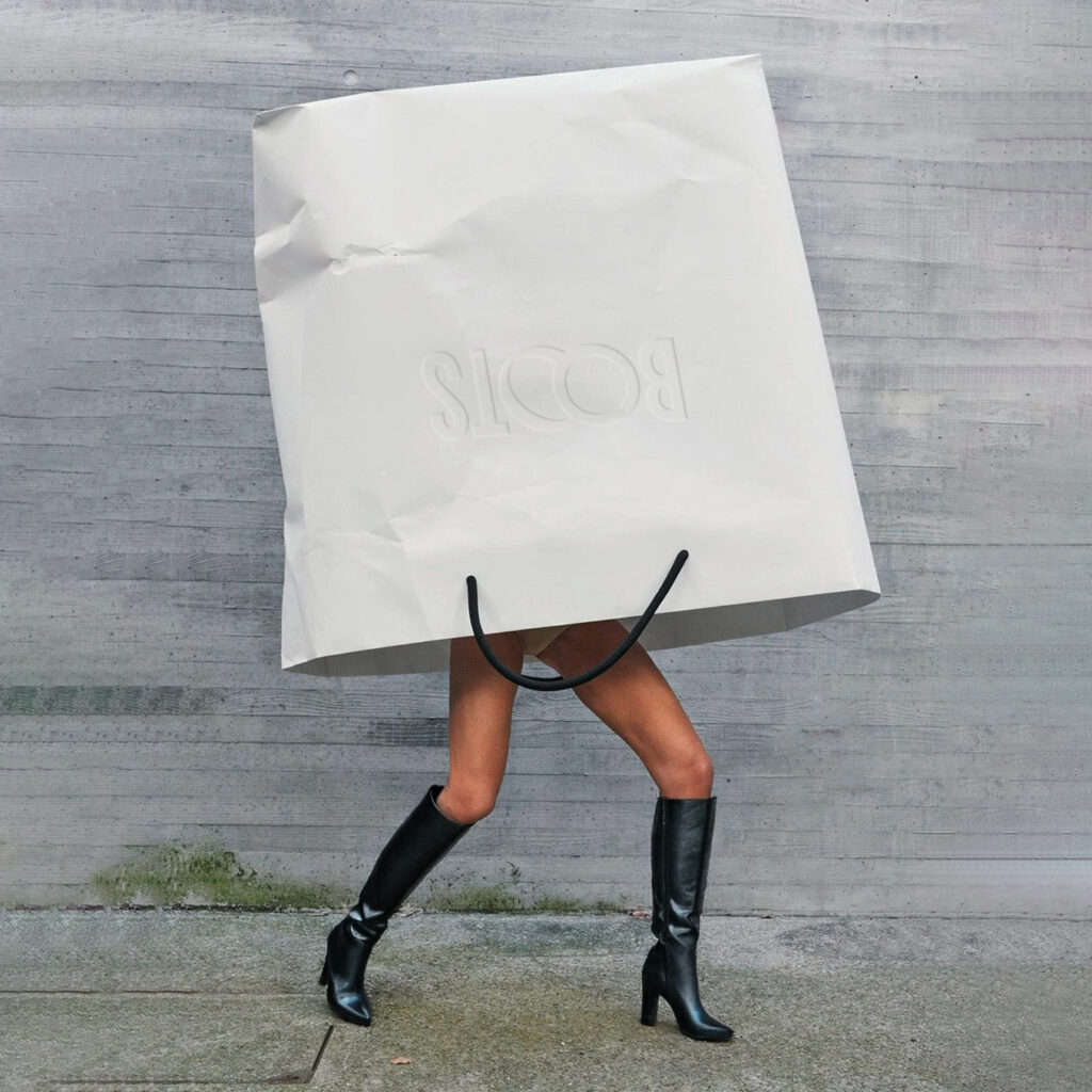 femme qui porte des bottes à talon noirs, avec un immense sac de shopping sur la tête de la marque Boots