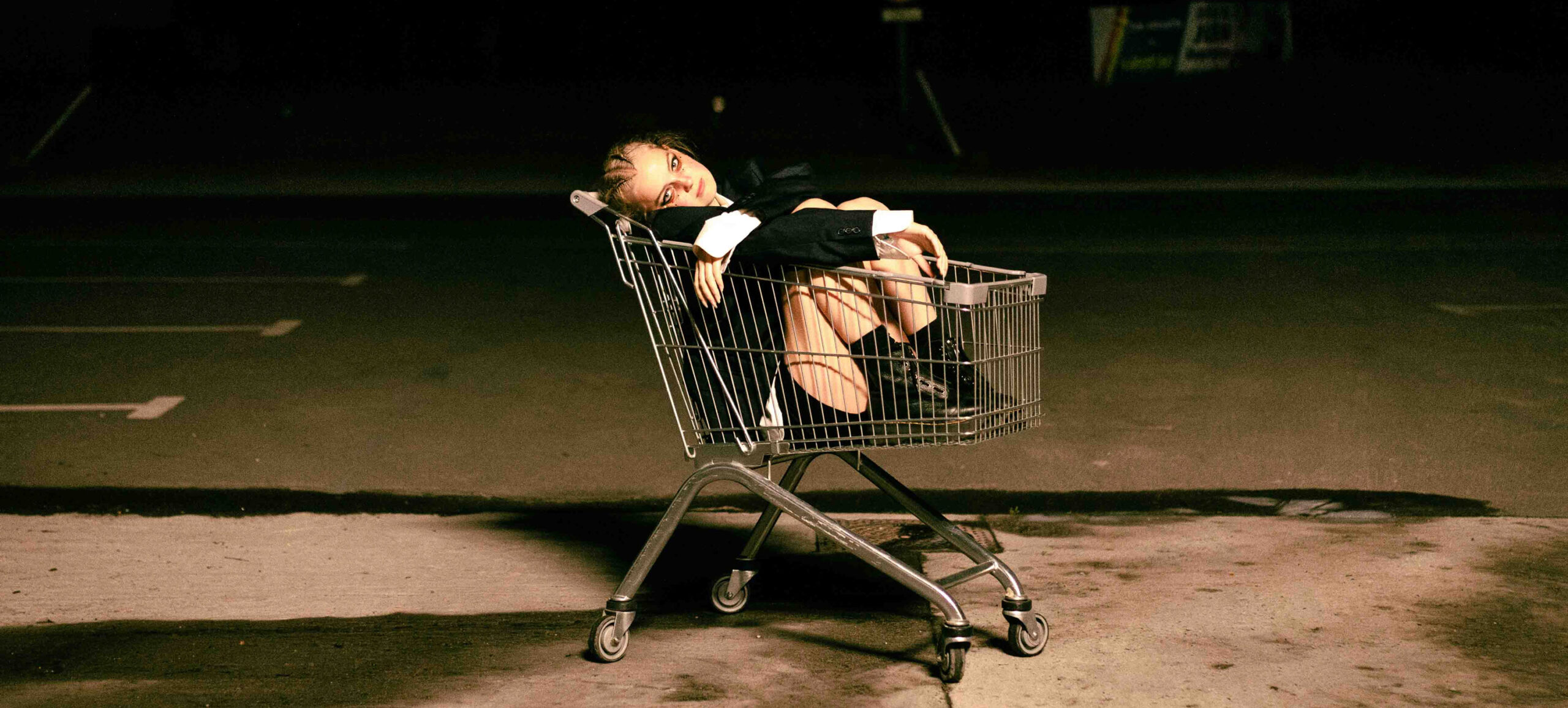Projet Court Métrange : photo d'une fille aux yeux maquillés de noir, avec des tresses blondes, ambiance gothique, assise dans un caddie de supermarché