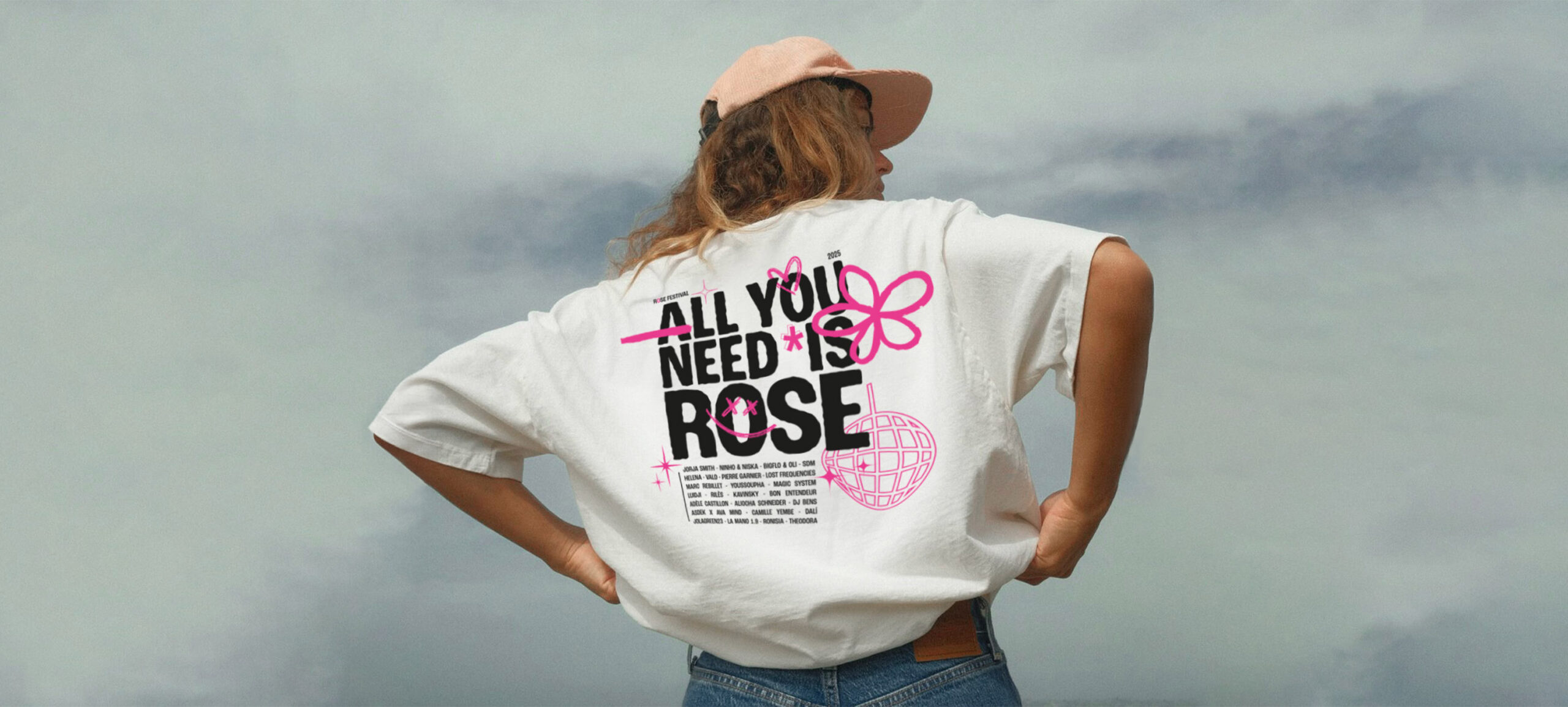 Projet Rose festival : femme de dos face au ciel, qui porte un tee-shirt avec le visuel proposé. Le visuel : la phrase "all you need is rose" en majuscule agrémentée de décorations (fleur, boule disco, smiley) roses